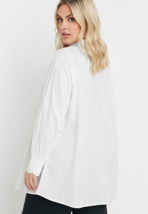 Camicia di lino bianca con maniche lunghe, polsini abbottonati e spacchi laterali. Presenta una vestibilità rilassata e un tessuto testurizzato.