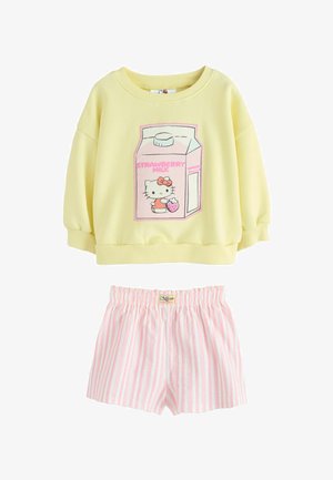 Gul langærmet top med Hello Kitty, der holder en jordbær på et lyserødt kartonprint, kombineret med lyserøde og hvide vertikalt stribede elastiske shorts.
