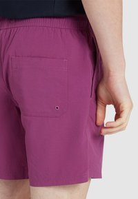 Paarse zwembroek met een achterzak met knoopsluiting, elastische tailleband en een lichte, gladde textuur.