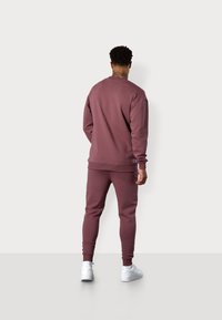 Kastanienbrauner Sweatshirt und passende Jogginghose, aus weichem Stoff gefertigt. Verfügt über gerippte Bündchen und einen elastischen Bund, kombiniert mit weißen Schuhen.