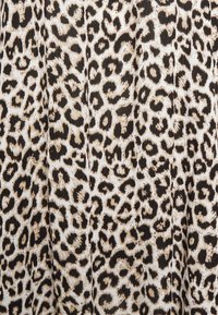 Tissu imprimé léopard beige et noir avec des taches texturées et irrégulières, présentant des plis doux dans le matériau.