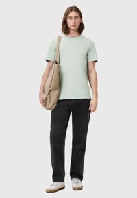 T-shirt in cotone verde chiaro, jeans neri e sneakers bianche. Borsa tote in cotone beige con un design sottile, indossata sulla spalla.