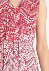 Robe à motifs rouges et blancs mettant en avant un design enroulé, une jupe plissée et un décolleté en V. Le tissu présente un aspect léger et texturé.