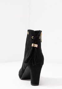 Zwarte suede enkellaarsjes met een hoge hak, voorzien van een franjerdetail en gouden hardware. Glad textuur en een afgeronde neusvorm.