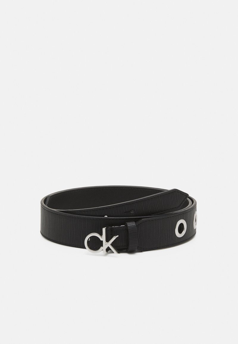 Ceinture en cuir noir avec boucle argentée "ck" et œillets ronds argentés, enroulée sur un fond blanc uni.