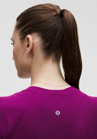 Lilla sporttop, millel on ribakujuline tekstuur; selja taga on väike logo; juuksed on pundud hobusesabasse.