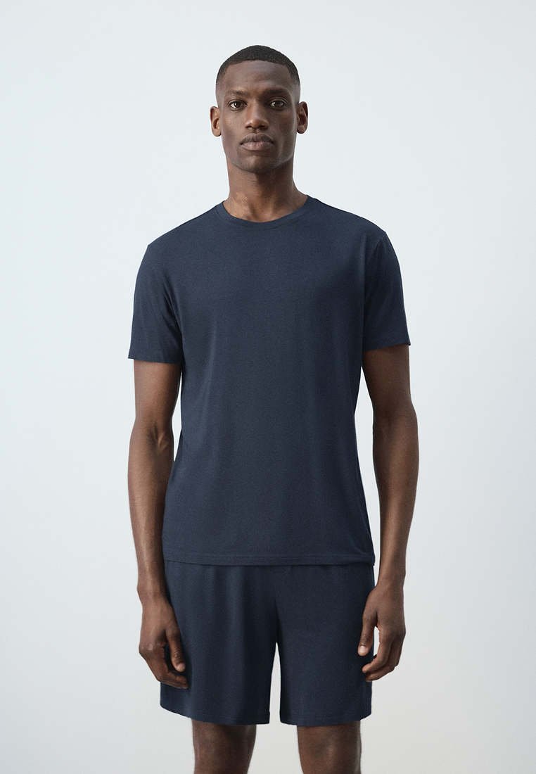 Homme debout face à l’avant portant un t-shirt à manches courtes bleu marine uni et un short assorti sur fond gris clair.