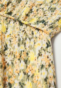 Tejido con estampado floral en tonos amarillos, verdes y blancos. Ligero, con textura plisada, acabado suave y detalles en forma de concha en los bordes.