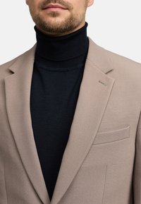 Beige blazer met een geknipte revers, textuurstof, enkele borstzak, gedragen over een zwarte coltrui. Minimalistisch ontwerp.