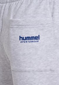 Pantalons de survêtement en coton gris avec une poche latérale, arborant un logo bleu "Hummel Sportswear". Texture douce avec un aspect légèrement chiné.