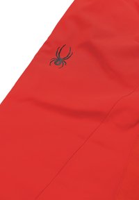 Indumento di tessuto rosso con una texture liscia, con un logo di ragno nero sul lato. Il design è slanciato con cuciture precise.