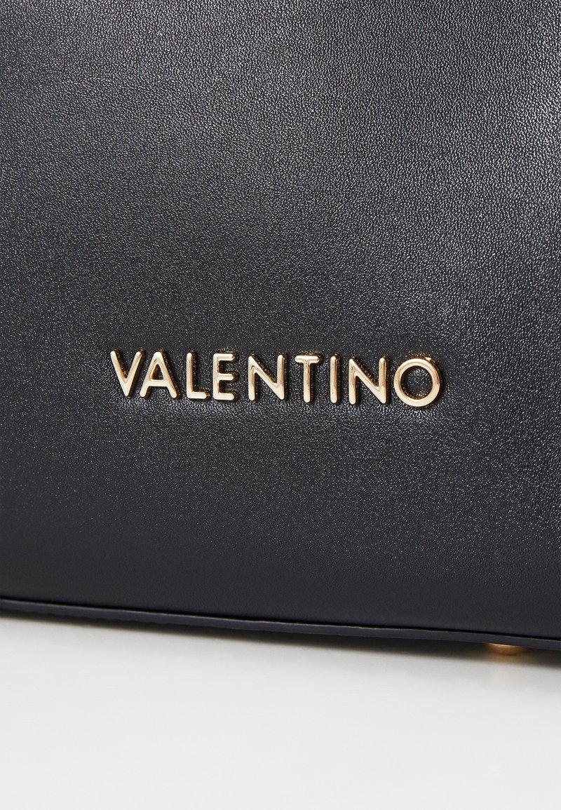 Sac en cuir noir texturé avec le logo en or "VALENTINO" embossé à l'avant, présentant une finition lisse et un design minimaliste.