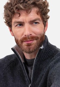 Pull gris foncé avec un col haut et une fermeture éclair à l'avant, présentant un design en tricot texturé et un intérieur gris plus clair.