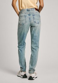 Gai zili džinsi ar pieguļošu siluetu, piecu kabatu dizainu un nelielu nodilumu. Iezīmē redzama šuvuma un brūnas ādas birka.