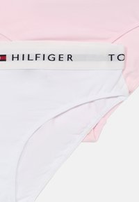 Divas divi pāri sieviešu apakšveļas: viens rozā un viens balts. Katrs izgatavots no mīksta kokvilnas materiāla un ar zīmola elastīgu jostu ar uzrakstu "HILFIGER".