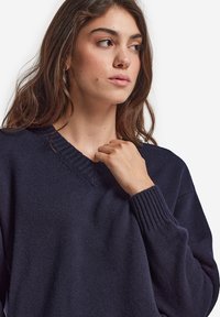 Marinblå, stickad tröja med V-ringning, ribbade muddar och en mjuk struktur; har en avslappnad passform och subtila sömnadsdetaljer.