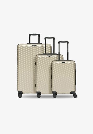 Tre valigie rigide beige con manici telescopici neri e quattro ruote, disposte in ordine decrescente di dimensione da sinistra a destra.