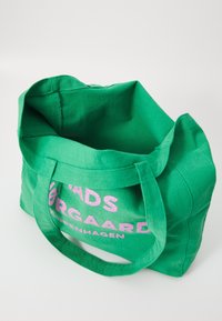 Sac fourre-tout en toile verte avec du texte rose indiquant "SADSD ØRGAARD COPENHAGUE." Il dispose de poignées robustes et d'un design spacieux et ouvert.