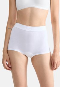Witte katoenen high-waisted onderbroek met een zachte tailleband en naadloos ontwerp, getoond op een persoon van de taille naar beneden.