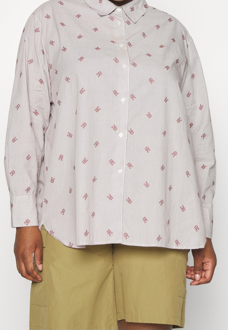 Personne portant une chemise ample à manches longues boutonnée avec un col et petits motifs rouges, associée à un short vert olive.