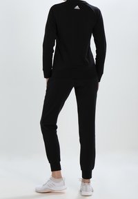 Czarny sportowy sweter z okrągłym dekoltem i ściągaczami, w zestawie z dopasowanymi dresami. Białe sneakersy z teksturowanym wzorem.