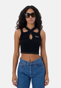 Zwarte cropped tanktop met een sleutelgat uitsnede, met kruisbanden en contrasterende stiksels. Gecombineerd met high-waisted blauwe spijkerbroek.