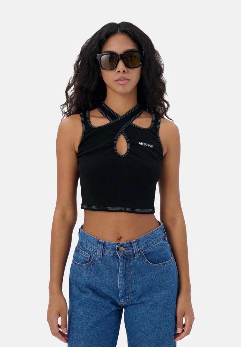 Zwarte cropped tanktop met een sleutelgat uitsnede, met kruisbanden en contrasterende stiksels. Gecombineerd met high-waisted blauwe spijkerbroek.