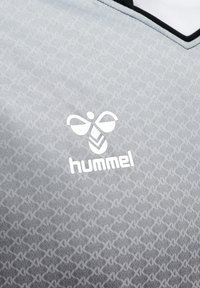 Szara sportowa koszulka z białym logo pszczoły hummel i powtarzającym się subtelnym wzorem szewronu, z czarno-białym kołnierzem w kształcie litery V.