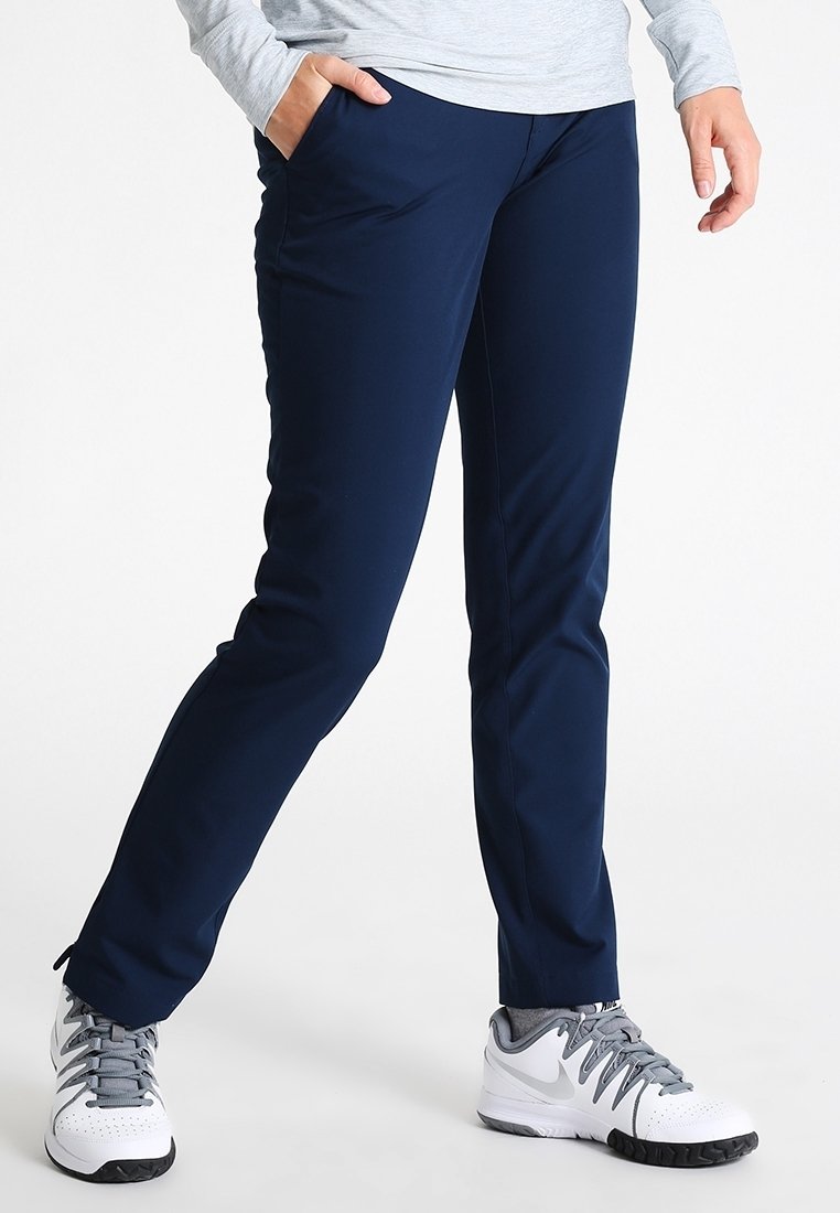 Mörkblå träningsbyxor med smal passform, tillverkade av ett stretchigt material. Har två sidofickor och bärs med vita träningsskor.