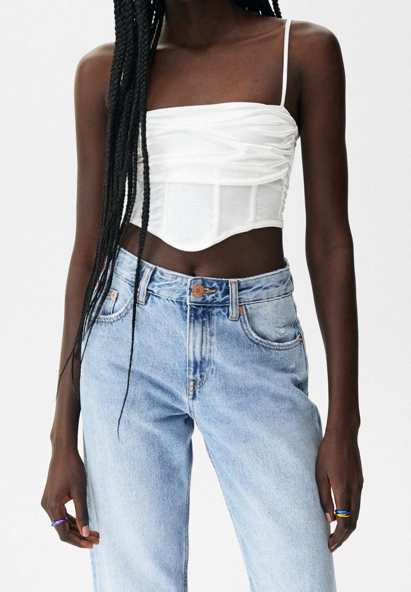 Witte strapless top met geplooide structuur, gecombineerd met lichtblauwe high-waisted jeans met een vervaagde afwerking en een klassiek vijf-pocket ontwerp.