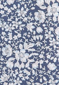 Motif floral blanc composé de diverses fleurs et feuilles sur un fond de tissu bleu texturé.
