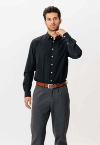 Sort langærmet skjorte med knapper og krave, lavet af glat stof. Kombineret med grå bukser og et brunt læderbælte.