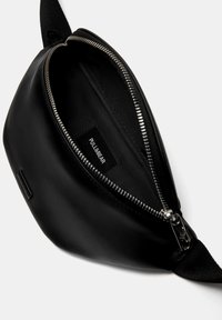 Crna torba od umjetne kože s srebrnim zatvaračem, s unutarnjom podstavom od tkanine i oznakom "PULL&BEAR" unutar. Glatka tekstura.