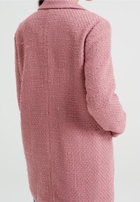 Rosa texturerad ullrock med krage och bak söm, med ett vävt mönster och något lös passform, når till mitten av låren.