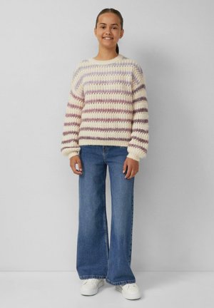 Strickpullover mit cremefarbener Basis und lila gestreiftem Muster, kombiniert mit blauen Schlagjeans und weißen Sneakers, vor einem hellen Hintergrund stehend.