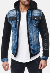 Denim en zwarte stoffen jacket met een ritssluiting, twee borstzakken en verweerde accenten. Met capuchon en bedrukte details op de mouwen.
