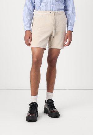Beige kordjerz shorts rugalmas derékkal és állítható zsinórral. Fekete cipővel és fehér bokazoknival párosítva.