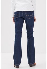 Tummansiniset leveälahkeiset farkut, joissa on sileä pinta. Huomiota herättävä tikkaus takataskuissa ja klassinen viiden taskun muotoilu.