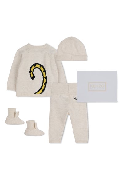 Kremowy zestaw ubranek dla niemowląt z sweterkiem pokazującym ogon tygrysa, pasującą czapką, spodniami, bucikami oraz pudełkiem z logo Kenzo.