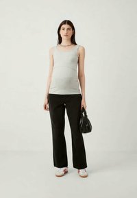 Γκρίζα ριγωτή αμάνικη μπλούζα, μαύρο παντελόνι με φαρδιά πόδια, λευκά sneakers με κόκκινες λεπτομέρειες και μαύρη τσάντα. Απλό φόντο.