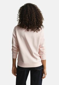 Felpa rosa chiaro con collo a giro, polsini e orlo a costine. Tessuto morbido e vestibilità comoda, abbinata a jeans denim scuri.