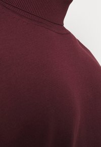 Pull en col roulé bordeaux en maille douce et texturée, avec un col et des coutures côtelés, et une silhouette ajustée.