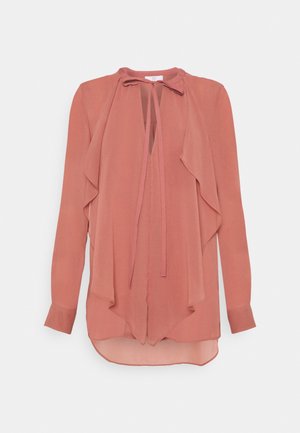 Lange mouwen stof rose blouse met ruches, een keyhole halslijn en striksluiting op een witte achtergrond.