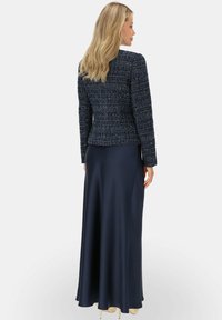 Granatowa tweedowa marynarka o teksturowanym materiale i usztywnionym kroju, zestawiona z zwiewną granatową satynową spódnicą, tworzy warstwowy wieczorowy look.