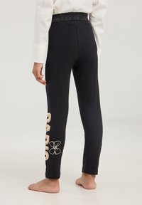 Pantaloni sportivi neri con una cintura elastica texturizzata e ricami decorativi color beige chiaro lungo la gamba sinistra, inclusi motivi floreali.