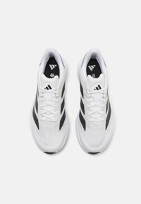 White athletic shoes with mesh upper, black diagonal stripes, and lace-up design. Features a padded collar and textured rubber sole.