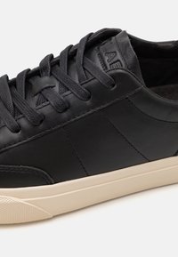Svart lær sneakers med en glatt finish, med runde svarte lisser, minimale sømdetaljer, og en kremfarget gummisåle.