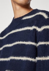 Mörkblå stickad tröja med vita mjuka horisontella ränder. Rund halsringning, mjuk textur och något avslappnad passform. Inga synliga logotyper eller mönster.