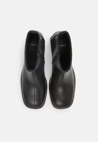 Botas de tobillo de cuero negro con un acabado suave, cremalleras laterales, puntera redondeada y detalles de costura sutiles en la parte superior. Suelas planas.