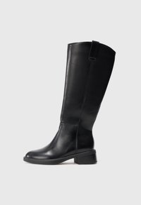 Botte en cuir noire jusqu'au genou avec un petit talon bloc et une anse en haut, présentée sur un fond clair et uni.